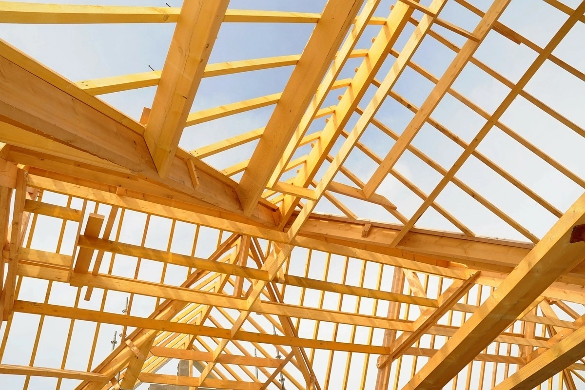 Structure de charpente en bois pour toiture sous un ciel bleu, montrant les chevrons et les poutres