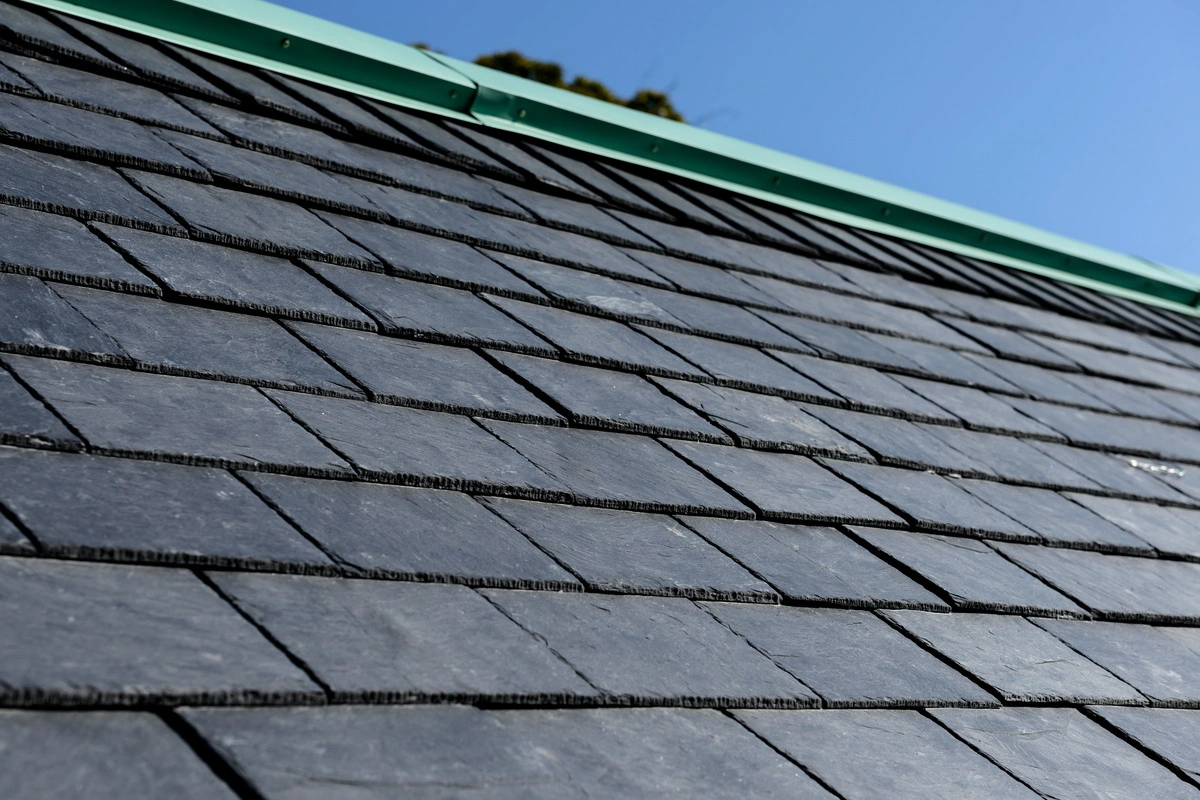 Toiture en ardoise sous un ciel bleu, montrant des tuiles en ardoise alignées avec précision