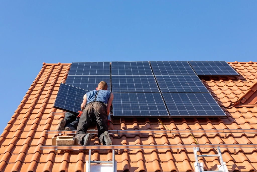 Couvreur installant des panneaux photovoltaïques sur une toiture en tuiles rouges